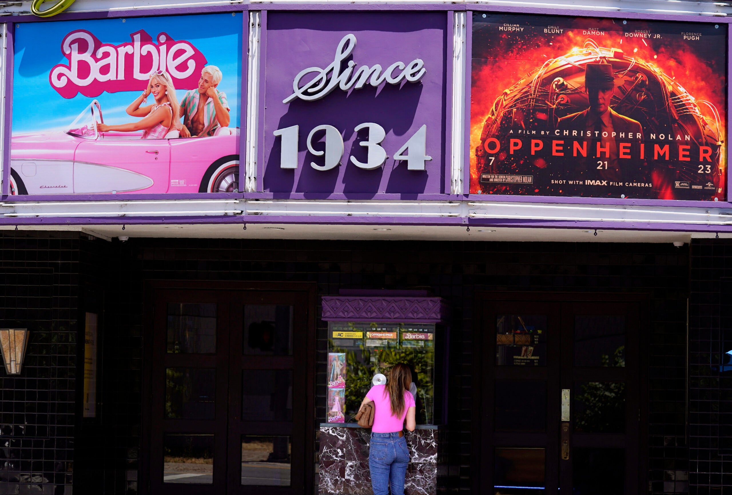 A patron buys a movie ticket underneath a marquee featuring the films "Barbie" and "Oppenheimer."
