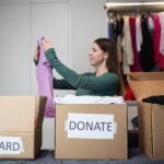 Unrecognizable woman sorts through her wardrobe. Three craft cardboard boxes of keep, discard, donation, donate. Charity clothing donations, help low income families, recycling, declutter, sustainable