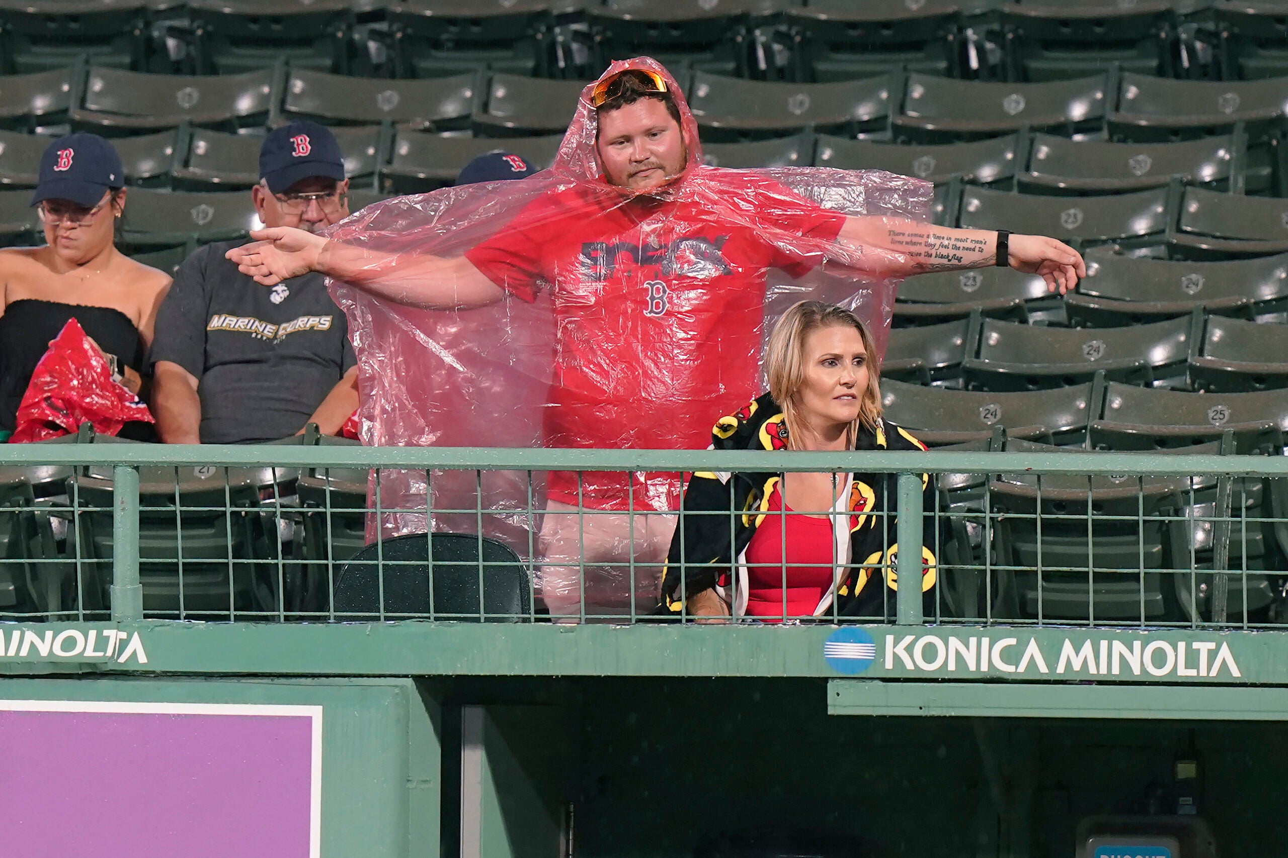 A Red Sox fan stretches as he puts on a red poncho during a rain delay .
